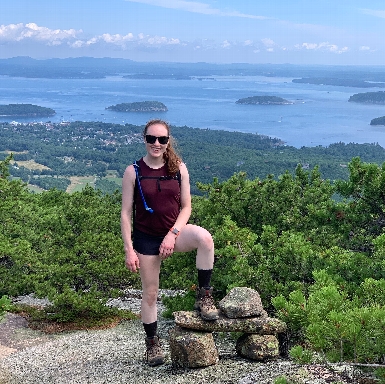 Laura joyously standing atop Dorr Mountain with beautiful views of Bar Harbor in the background.